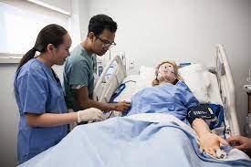 nurses practicing their craft in a stimulation lab, on a mannequin placed on a hospital bed.