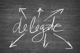 The word "delegate" written in chalk on a blackboard, with arrows pointing outwards, representing the concept of assigning tasks or responsibilities. 
