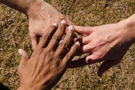 A diverse group of individuals standing in a sandy area, united as they hold hands together.