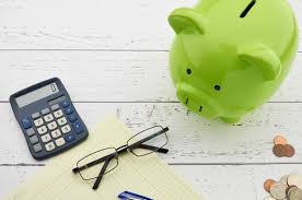 green piggy bank on a sheet of paper along with spectacles and a calculator