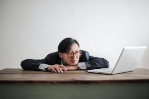 A man wearing glasses rests his head on a table, appearing tired or deep in thought.