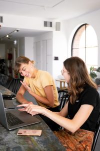 Two women working on laptops at a table, engrossed in their tasks.