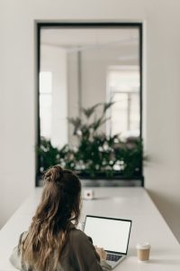 A woman sitting at a desk, working on a laptop and enjoying a cup of coffee.