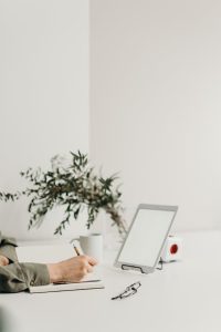 A focused woman sitting at a desk, diligently writing in a notebook with a pen.