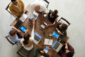 A diverse group of individuals sitting around a table, engrossed in their work on laptops.