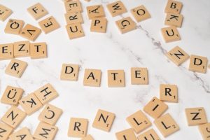 Scrabble tiles spelling "date" on a wooden surface.