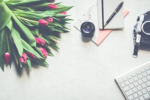 A desk adorned with a flower bouquet, camera, notebook, and laptop, creating a harmonious arrangement.