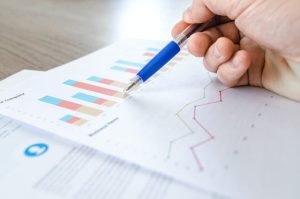 A hand holding a pen, examining a graph on paper.