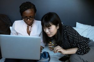 Two women on a bed, engrossed in a laptop.