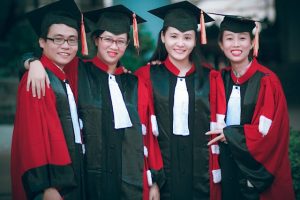 Four graduates in red and black robes posing for a photo.