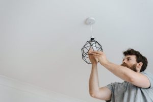  A man holding a light fixture, preparing to install it in a room.