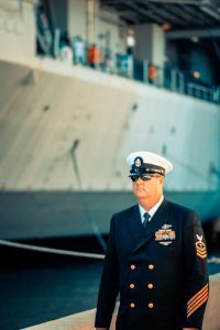 An officer in uniform posing confidently in front of a ship.